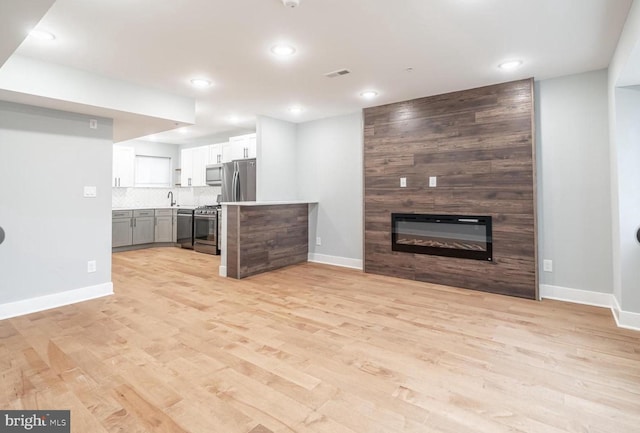 unfurnished living room featuring sink, a fireplace, and light hardwood / wood-style floors