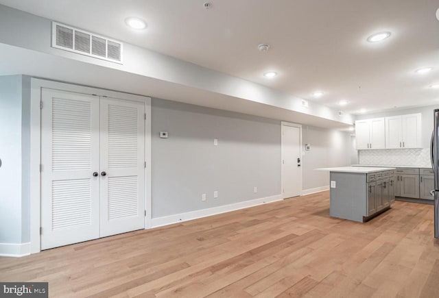 kitchen with gray cabinets, white cabinetry, backsplash, light hardwood / wood-style floors, and a kitchen island