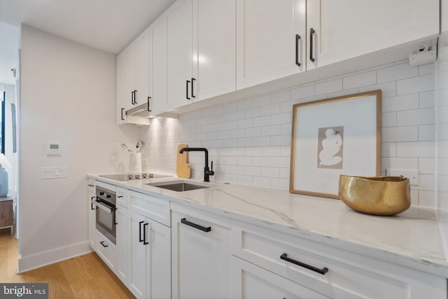 kitchen with white cabinetry, oven, sink, and light stone counters