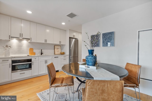 kitchen with sink, white cabinetry, tasteful backsplash, light wood-type flooring, and stainless steel appliances