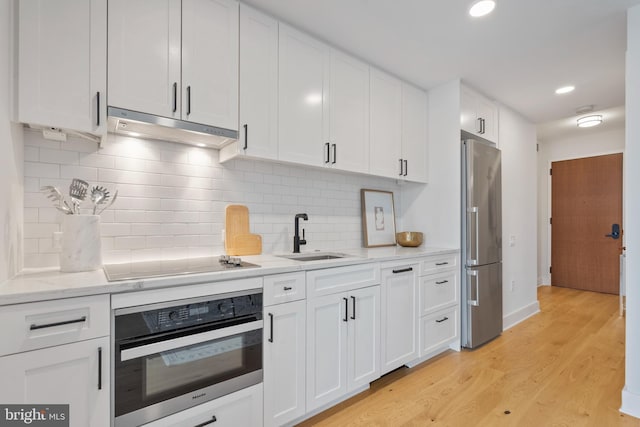 kitchen with appliances with stainless steel finishes, white cabinetry, sink, light stone counters, and light hardwood / wood-style floors