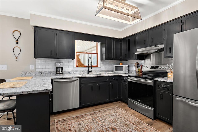 kitchen featuring sink, light wood-type flooring, ornamental molding, appliances with stainless steel finishes, and a kitchen breakfast bar