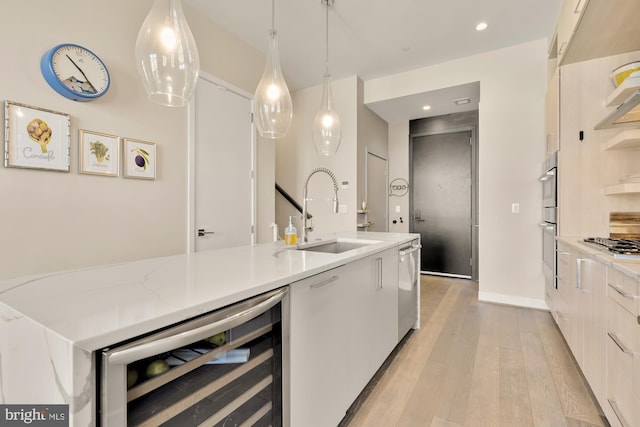 kitchen featuring sink, light stone countertops, decorative light fixtures, beverage cooler, and light wood-type flooring