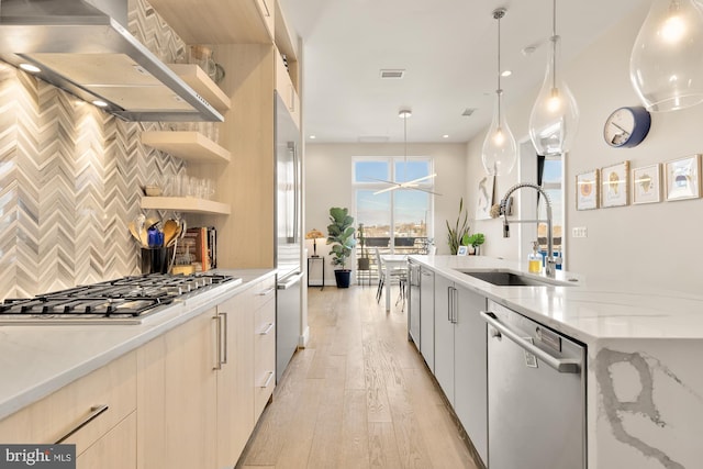 kitchen featuring sink, range hood, stainless steel appliances, light stone counters, and decorative light fixtures