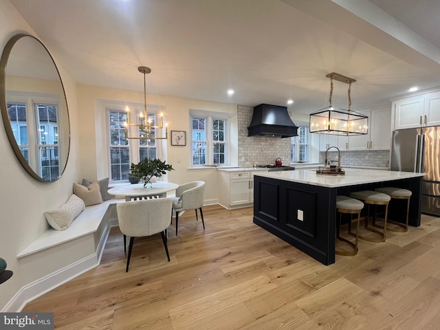 kitchen with appliances with stainless steel finishes, a kitchen island, decorative light fixtures, white cabinetry, and custom range hood