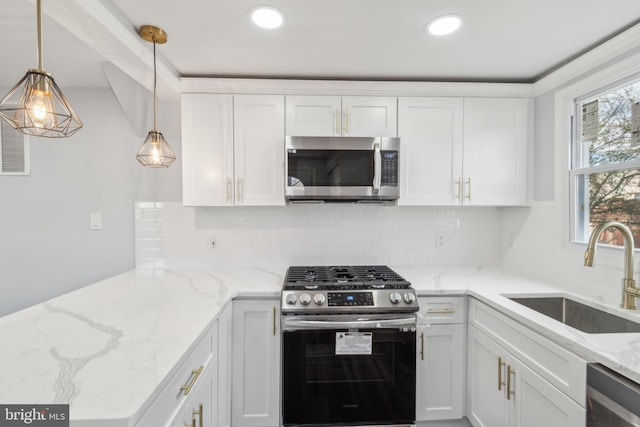 kitchen with appliances with stainless steel finishes, sink, white cabinets, and decorative light fixtures