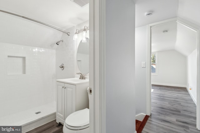 bathroom with vaulted ceiling, wood-type flooring, vanity, tiled shower, and toilet