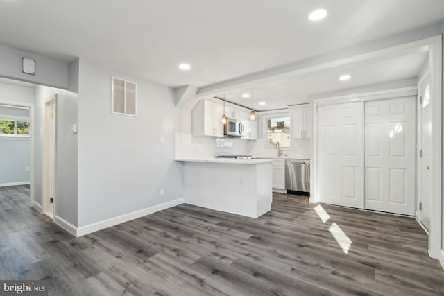 kitchen with pendant lighting, appliances with stainless steel finishes, white cabinetry, dark hardwood / wood-style flooring, and kitchen peninsula