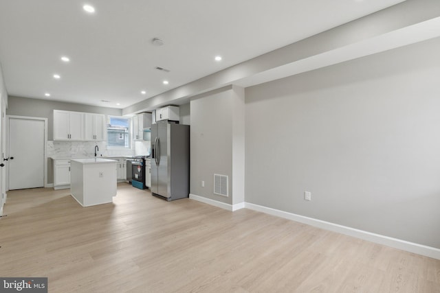 kitchen featuring appliances with stainless steel finishes, white cabinetry, backsplash, a center island, and light hardwood / wood-style floors