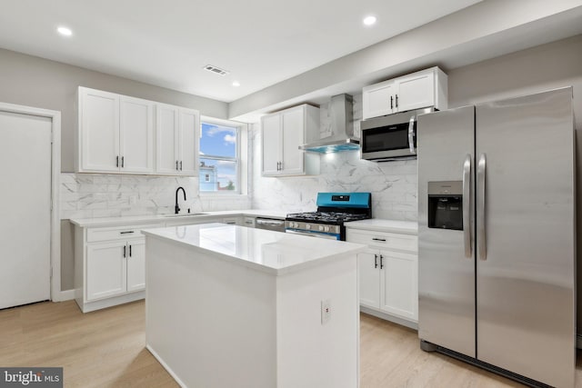 kitchen featuring white cabinetry, stainless steel appliances, a center island, and wall chimney exhaust hood