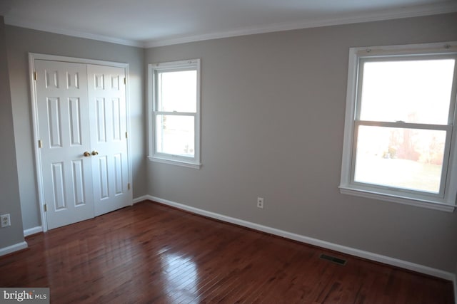 unfurnished bedroom featuring dark wood-type flooring, ornamental molding, and a closet