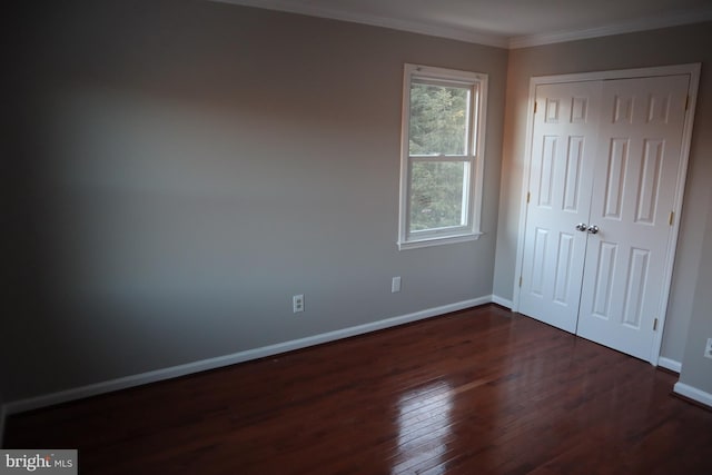 unfurnished bedroom with crown molding, dark wood-type flooring, and a closet