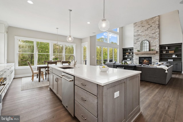 kitchen featuring a stone fireplace, an island with sink, sink, dark hardwood / wood-style flooring, and hanging light fixtures