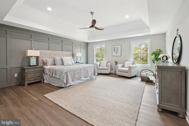 bedroom with dark wood-type flooring, ceiling fan, and a tray ceiling