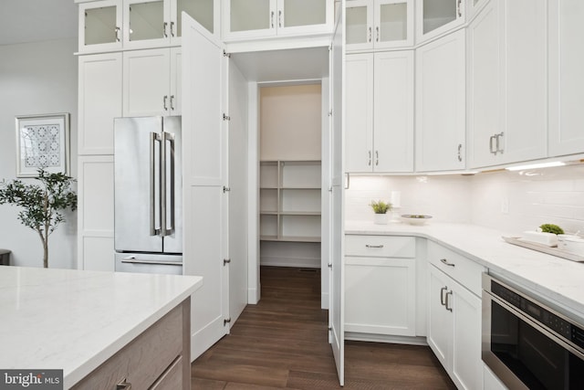 kitchen featuring high quality fridge, white cabinets, light stone counters, and decorative backsplash