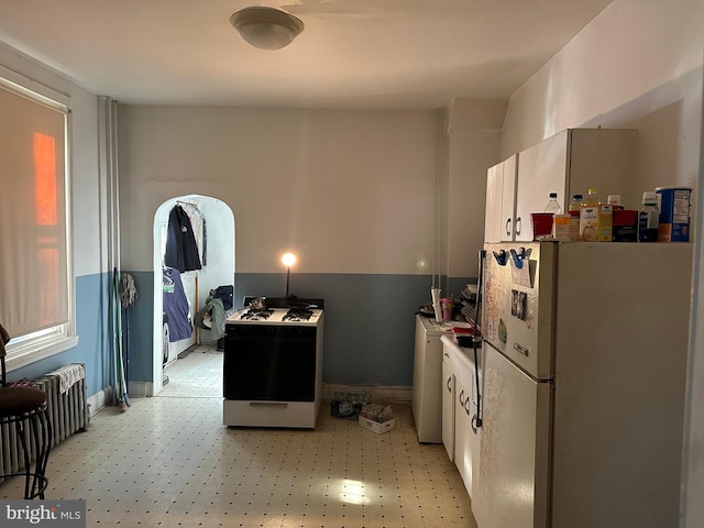 kitchen featuring radiator heating unit, gas range oven, white cabinets, and white fridge