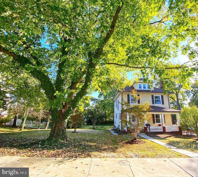 view of front of house featuring covered porch, a front lawn, and fence