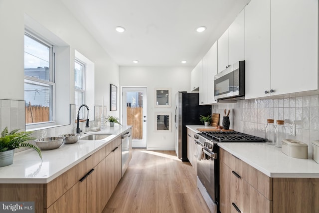 kitchen featuring sink, white cabinetry, stainless steel appliances, tasteful backsplash, and light hardwood / wood-style floors