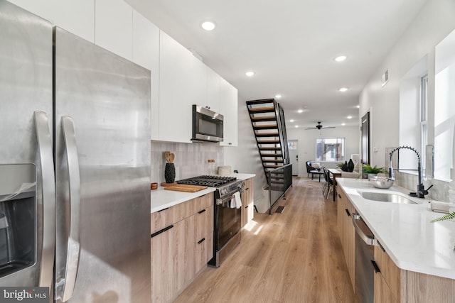 kitchen with sink, stainless steel appliances, tasteful backsplash, white cabinets, and light wood-type flooring