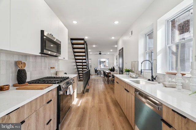 kitchen with sink, white cabinetry, appliances with stainless steel finishes, light hardwood / wood-style floors, and decorative backsplash