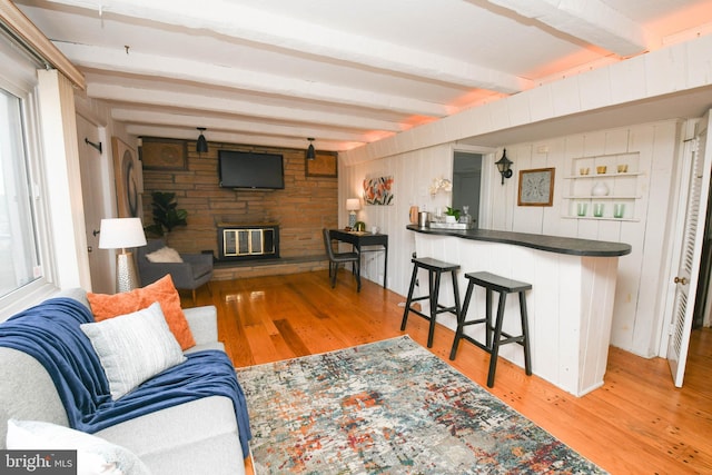 living room with bar area, beam ceiling, a fireplace, and light wood-type flooring