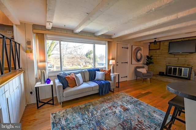 living room featuring wood-type flooring, a stone fireplace, beam ceiling, and a textured ceiling