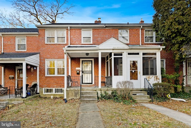 townhome / multi-family property featuring covered porch, brick siding, and a chimney