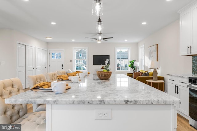 kitchen featuring pendant lighting, a kitchen island, light stone counters, white cabinets, and a kitchen bar