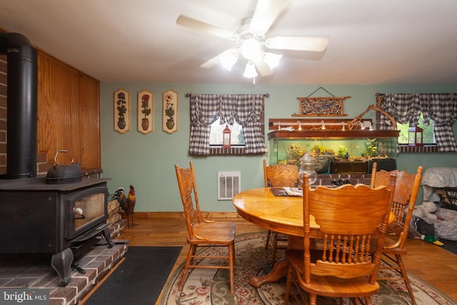 dining area with a wood stove, hardwood / wood-style floors, and ceiling fan