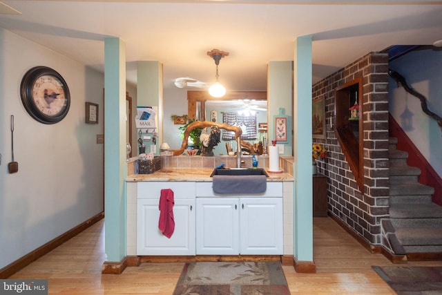 kitchen with white cabinetry, decorative light fixtures, sink, and light hardwood / wood-style flooring