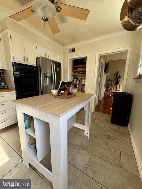 kitchen with crown molding, black oven, ceiling fan, stainless steel refrigerator with ice dispenser, and white cabinets