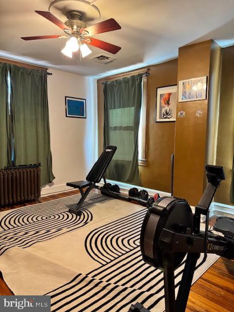 workout area with ceiling fan, wood-type flooring, and radiator