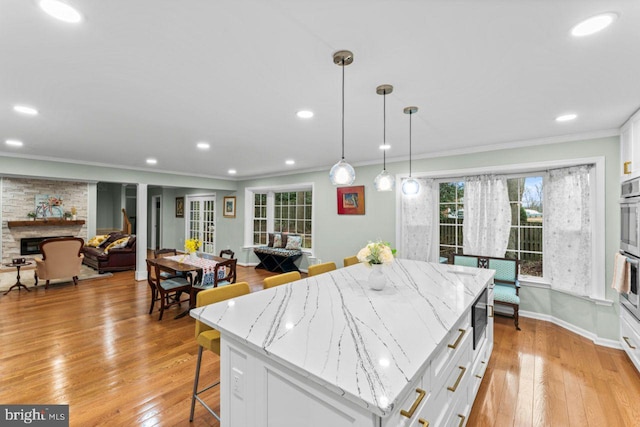 kitchen featuring white cabinetry, hanging light fixtures, a center island, a fireplace, and light stone countertops