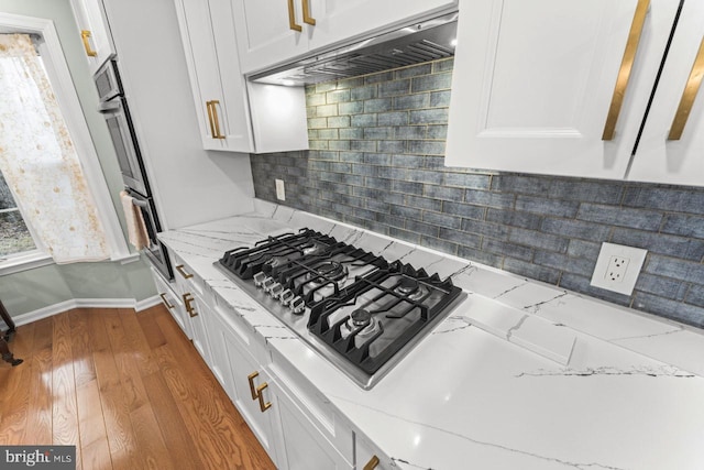 kitchen with exhaust hood, light stone counters, appliances with stainless steel finishes, light hardwood / wood-style floors, and white cabinets