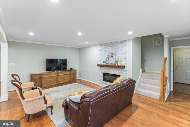 living room with crown molding, a stone fireplace, and light hardwood / wood-style flooring