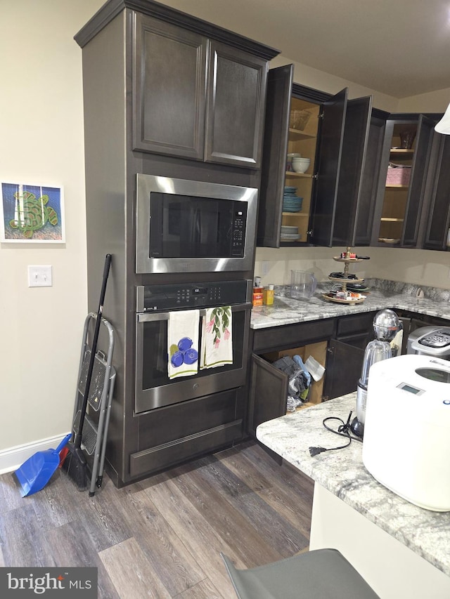 kitchen with dark brown cabinetry, appliances with stainless steel finishes, hardwood / wood-style floors, and light stone counters