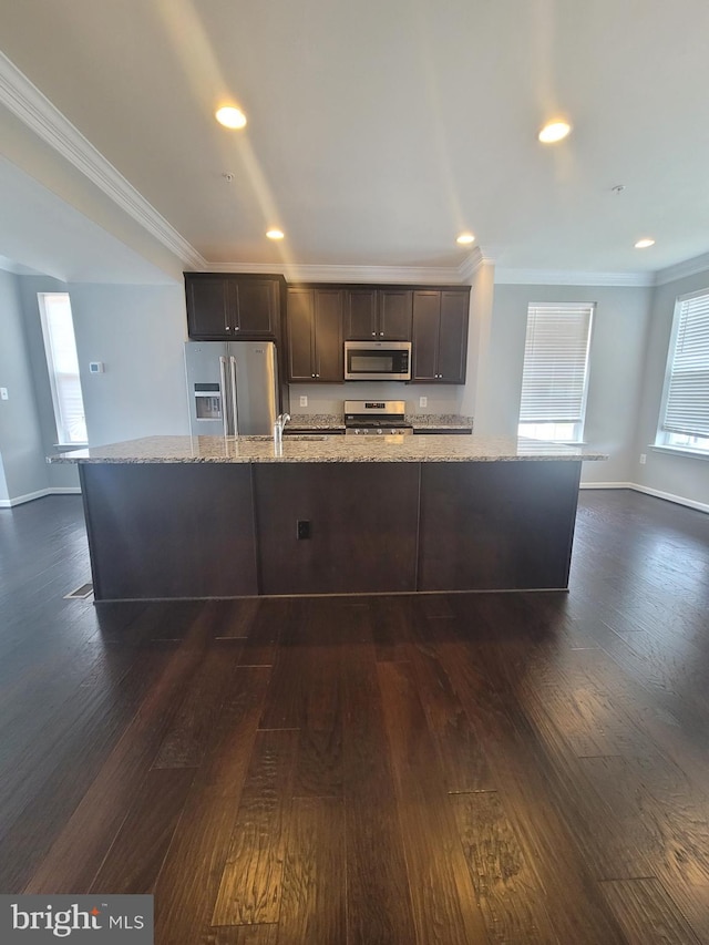 kitchen with a kitchen island with sink, light stone counters, dark brown cabinets, and appliances with stainless steel finishes