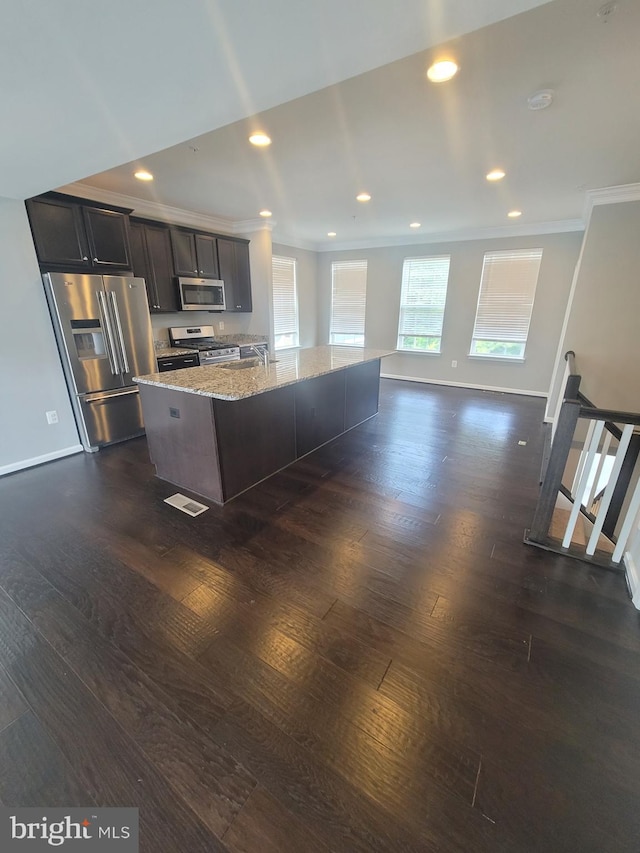 kitchen with dark wood-type flooring, light stone counters, dark brown cabinets, stainless steel appliances, and a kitchen island with sink