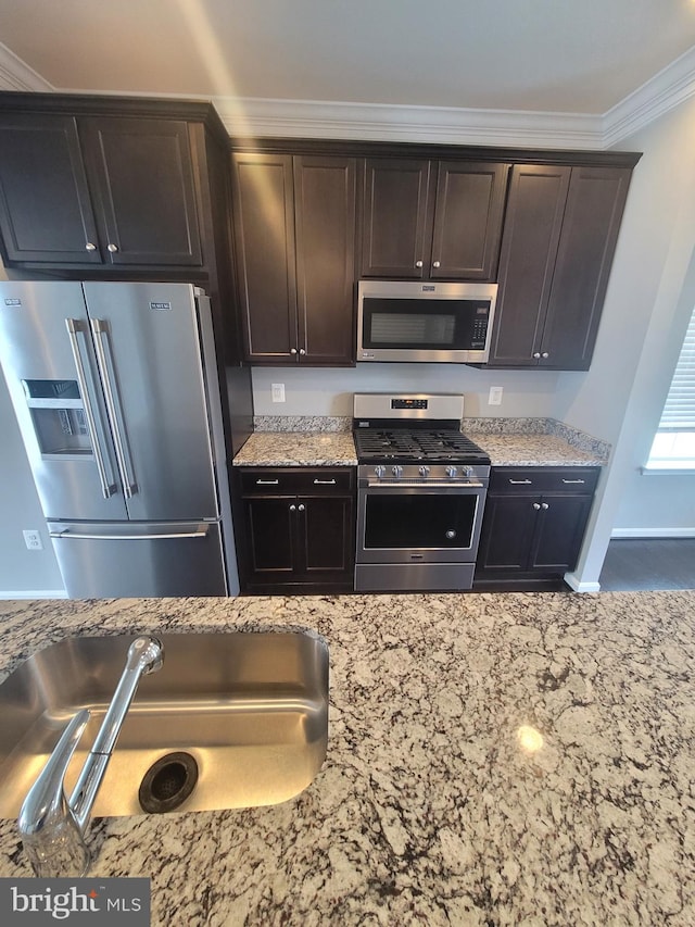 kitchen with ornamental molding, appliances with stainless steel finishes, light stone counters, and dark brown cabinetry