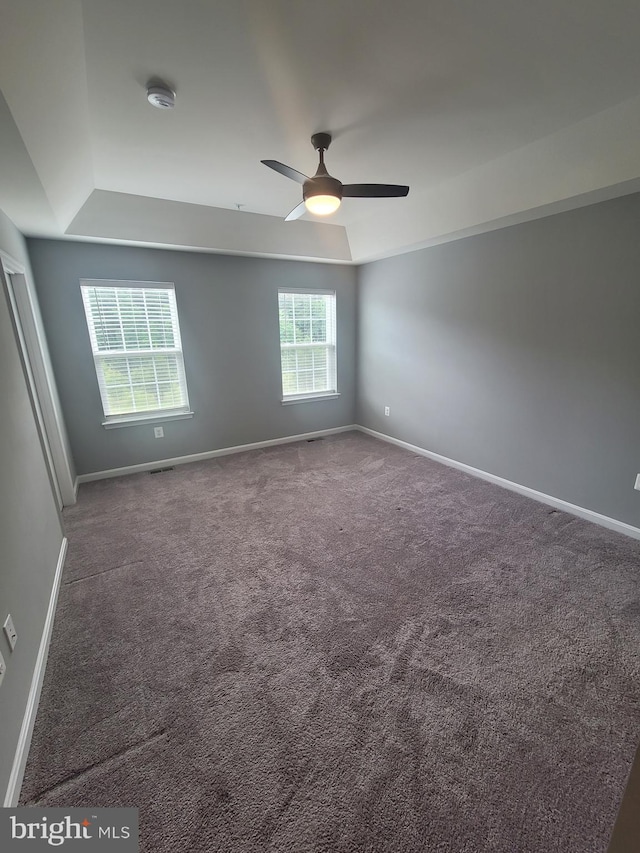 carpeted empty room featuring ceiling fan and a raised ceiling