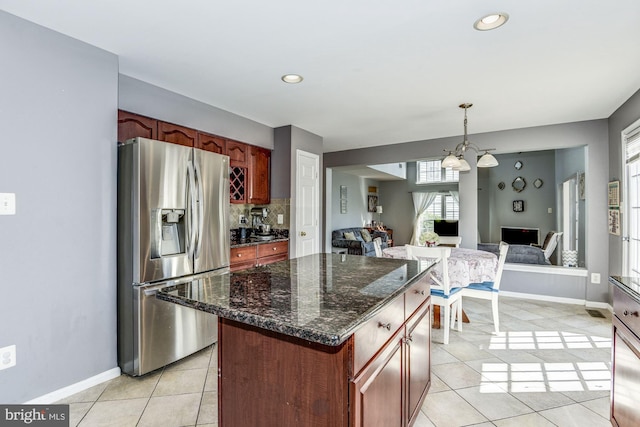 kitchen featuring stainless steel refrigerator with ice dispenser, decorative light fixtures, dark stone countertops, light tile patterned floors, and decorative backsplash