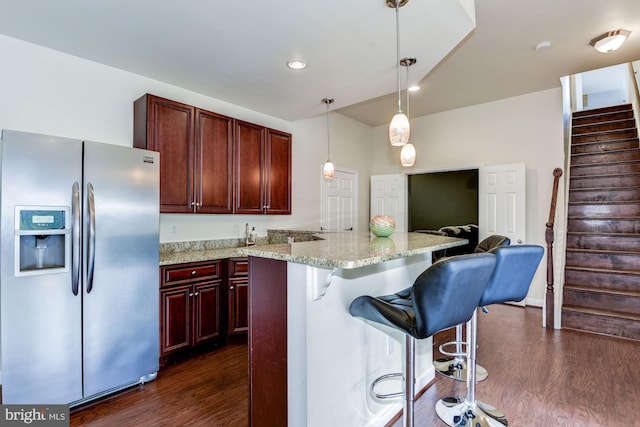 kitchen featuring a kitchen breakfast bar, hanging light fixtures, stainless steel fridge with ice dispenser, light stone countertops, and dark wood-type flooring