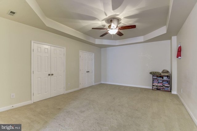 unfurnished bedroom featuring ceiling fan, light colored carpet, a raised ceiling, and multiple closets