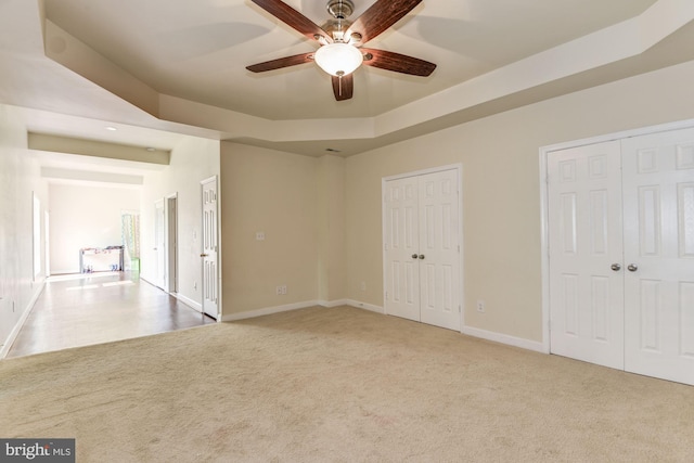 spare room with light colored carpet, a raised ceiling, and ceiling fan