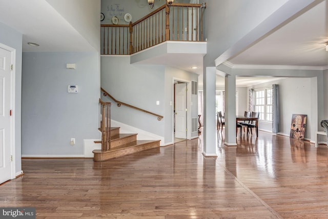 entrance foyer featuring a towering ceiling, wood-type flooring, and ornamental molding