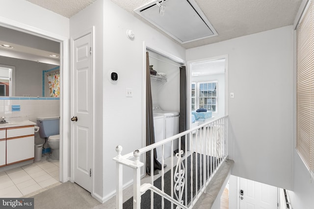 hallway featuring sink, tile walls, washer and dryer, a textured ceiling, and light tile patterned flooring