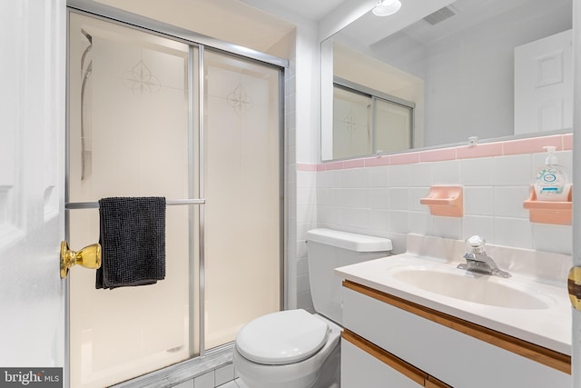 bathroom with a shower with door, vanity, tile walls, and toilet