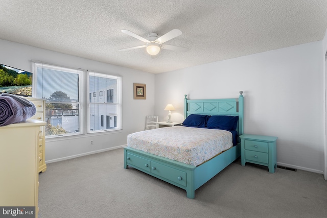 bedroom with ceiling fan, light colored carpet, and a textured ceiling