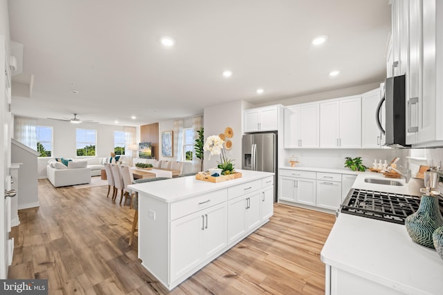 kitchen featuring a kitchen island, appliances with stainless steel finishes, white cabinets, ceiling fan, and light wood-type flooring