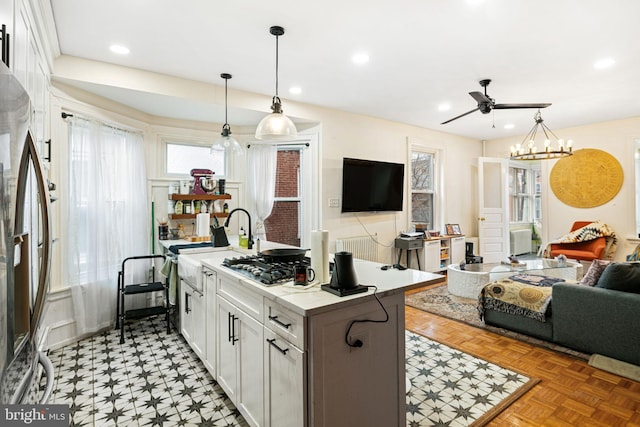 kitchen with appliances with stainless steel finishes, white cabinets, hanging light fixtures, light parquet flooring, and a center island with sink